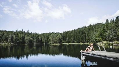 Woman relaxing on dock by calm forest lake on sunny day
