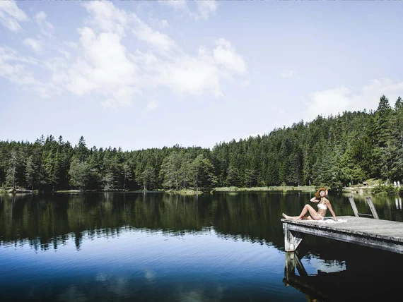 Woman relaxing on dock by calm forest lake on sunny day