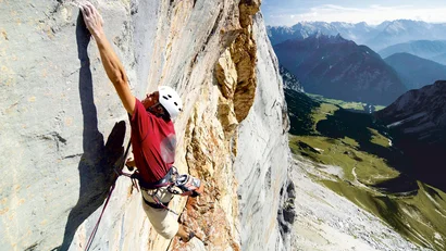Climber on steep rock face with mountain landscape in background