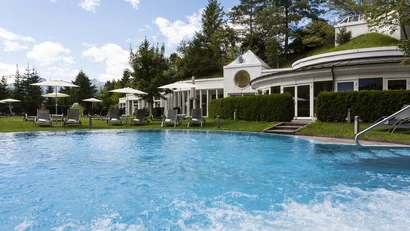 Outdoor pool with lounge chairs and umbrellas by modern building surrounded by trees
