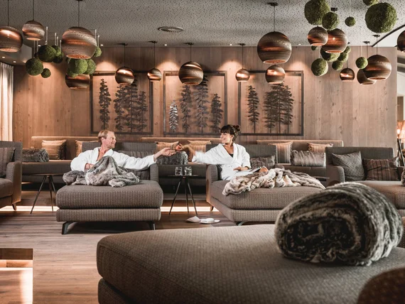 Two people relaxing in a cozy lounge with hanging lights and wooden decor.