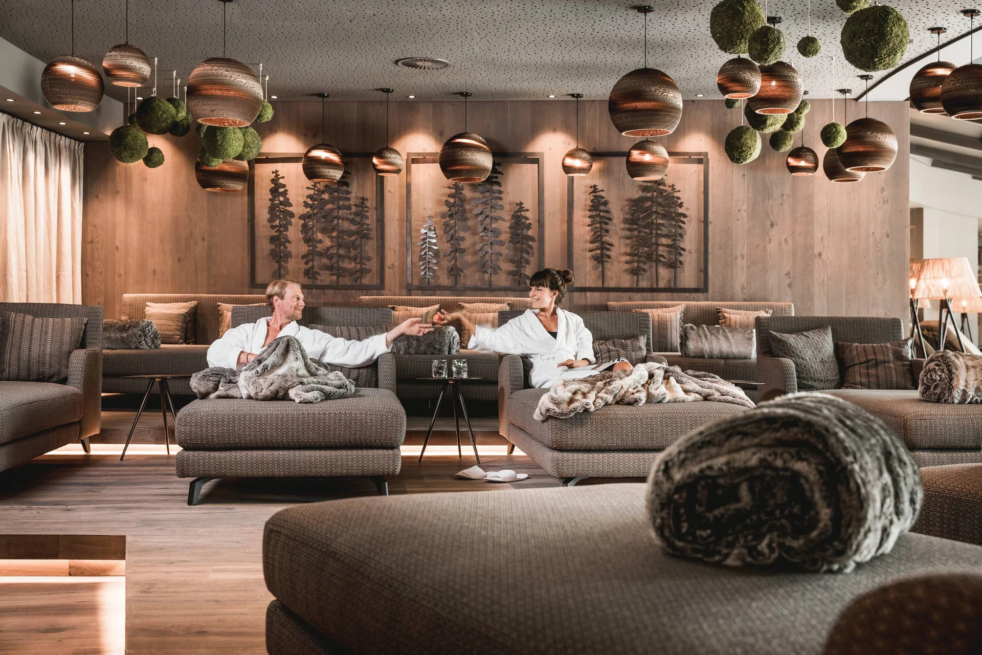 Two people relaxing in a cozy lounge with hanging lights and wooden decor.