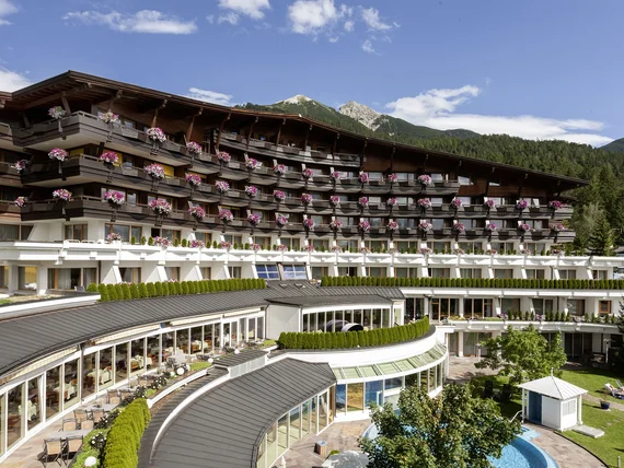 Hotel building with balconies, flowers, and mountain view under a clear sky