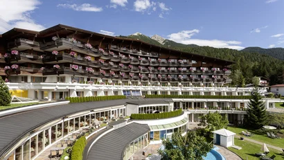 Hotel building with balconies, flowers, and mountain view under a clear sky
