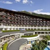 Hotel building with balconies, flowers, and mountain view under a clear sky
