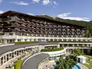 Hotel building with balconies, flowers, and mountain view under a clear sky