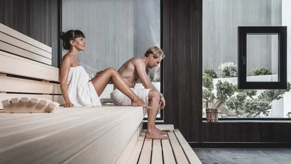 Man and woman relaxing in modern sauna with large windows