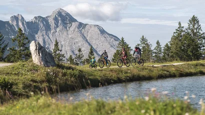 Family cycling on mountain trail with mountains and lake in the background