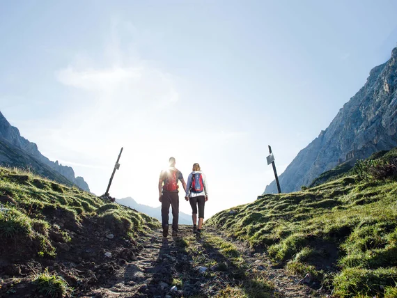A couple hiking on a rocky path between green mountains at sunrise
