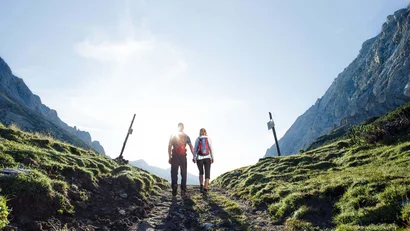 A couple hiking on a rocky path between green mountains at sunrise