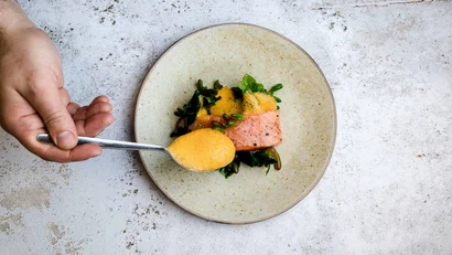 Hand spooning sauce over salmon and greens on a plate