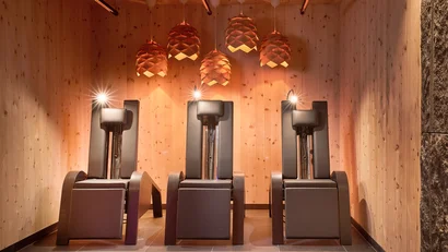 Five black massage chairs in a wooden room with hanging lamps