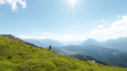 Hiker on green hill with mountain view under bright sky