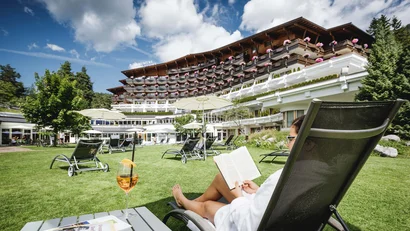 Person reading on lounge chair in front of hotel with flower balconies and blue sky