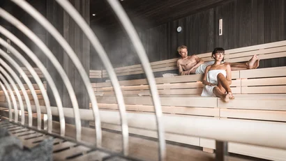 Two people relaxing in a modern wooden sauna with steam