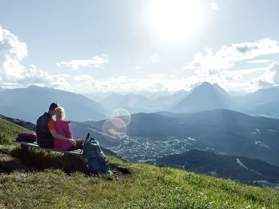 Couple sitting on bench overlooking sunny mountain landscape with clouds