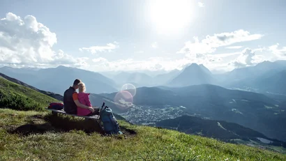 Couple sitting on bench overlooking sunny mountain landscape with clouds