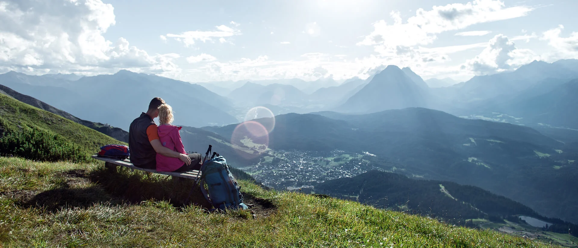 Couple sitting on bench overlooking sunny mountain landscape with clouds