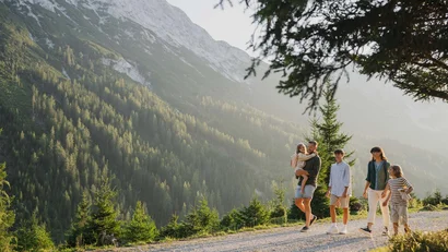 Family hiking on mountain trail with pine trees and rocky mountains behind
