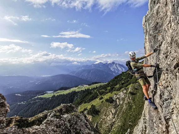 Climber on steep rock face with mountain landscape in the background