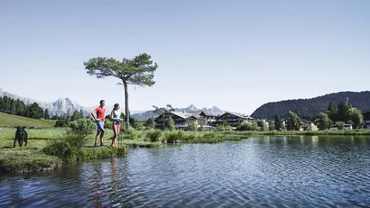 Couple by lake with mountain view and traditional buildings under clear blue sky