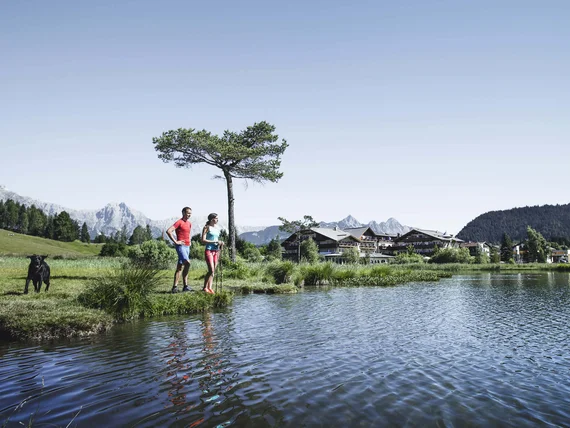 Couple by lake with mountain view and traditional buildings under clear blue sky