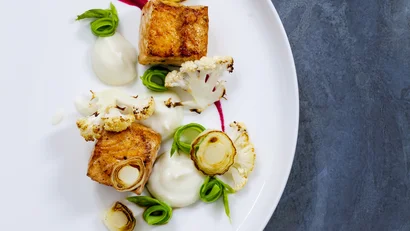 Gourmet dish with grilled fish, cauliflower, and colorful sauces on white plate