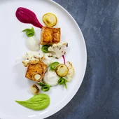 Gourmet dish with grilled fish, cauliflower, and colorful sauces on white plate