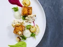 Gourmet dish with grilled fish, cauliflower, and colorful sauces on white plate