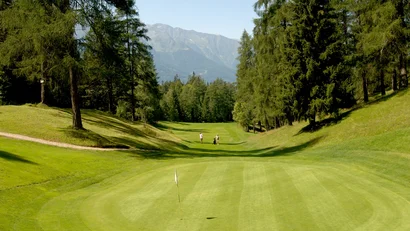 Golf course with players, surrounded by trees and mountains in the background