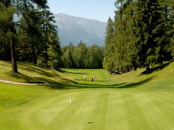 Golf course with players, surrounded by trees and mountains in the background
